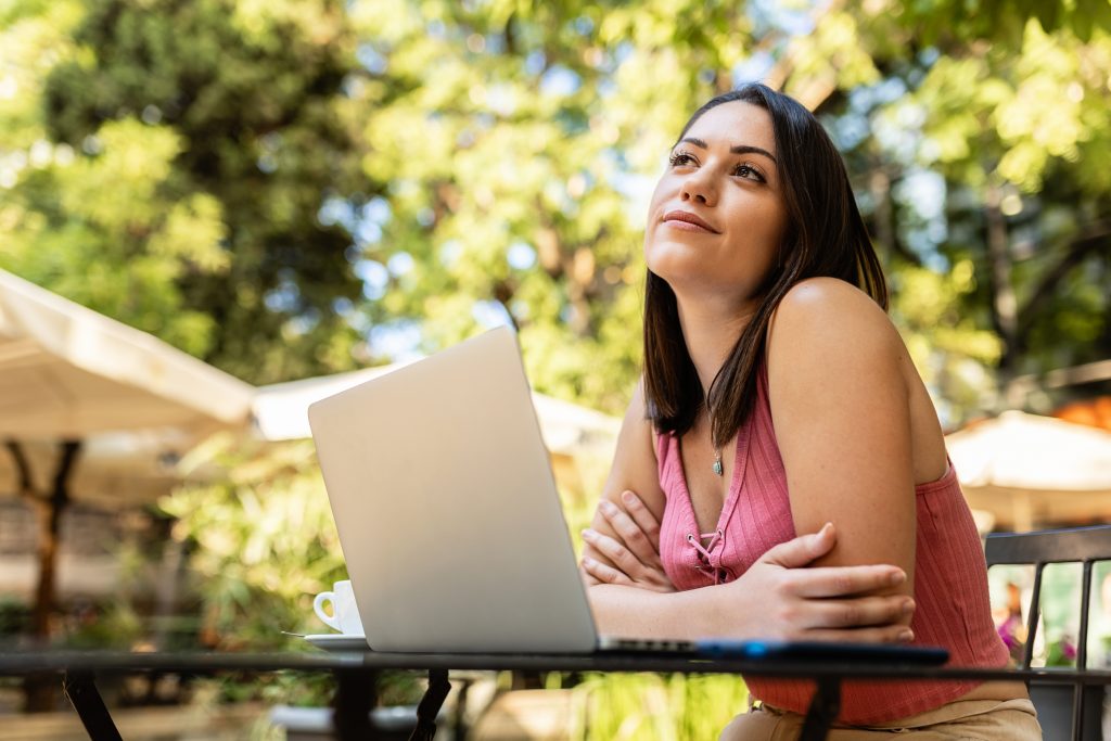 A woman sitting at an outdoor table with a laptop.